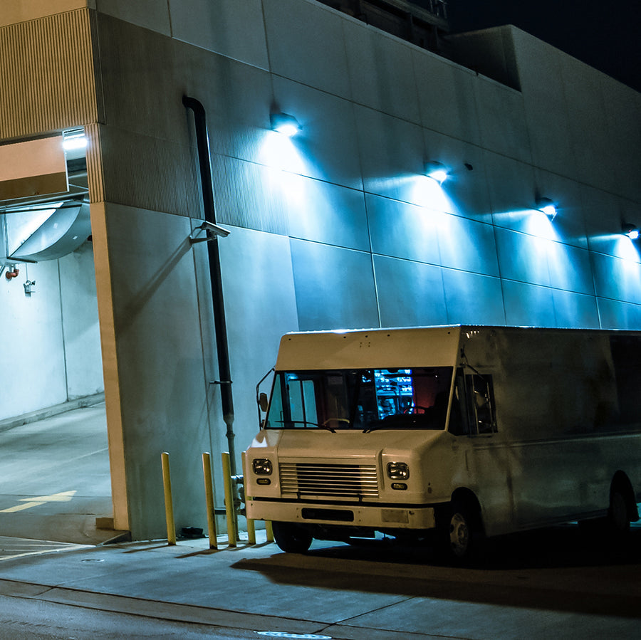 White van parked outside a building at night with blue lights on the wall.