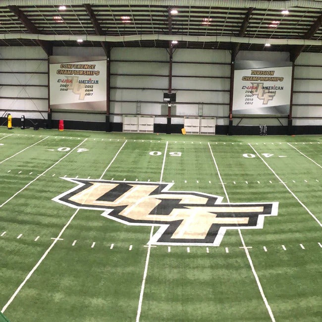 Indoor sports facility with a football field featuring UCF logo