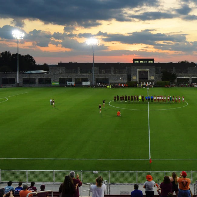 Soccer match on a field with players lined up for a penalty kick at sunset.